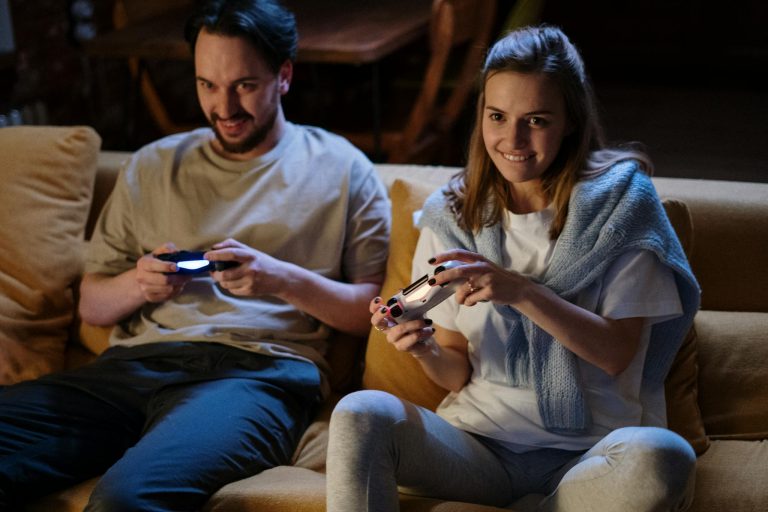 Young couple sitting on a sofa playing video games together in a warm, low-lit living room