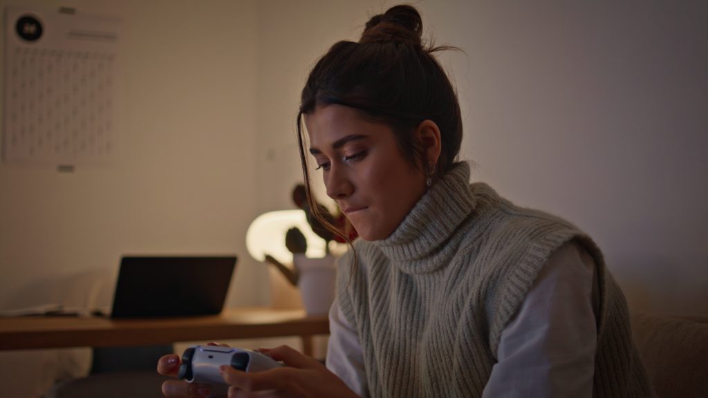 Woman in a cozy sweater concentrating while playing video games at home in the evening