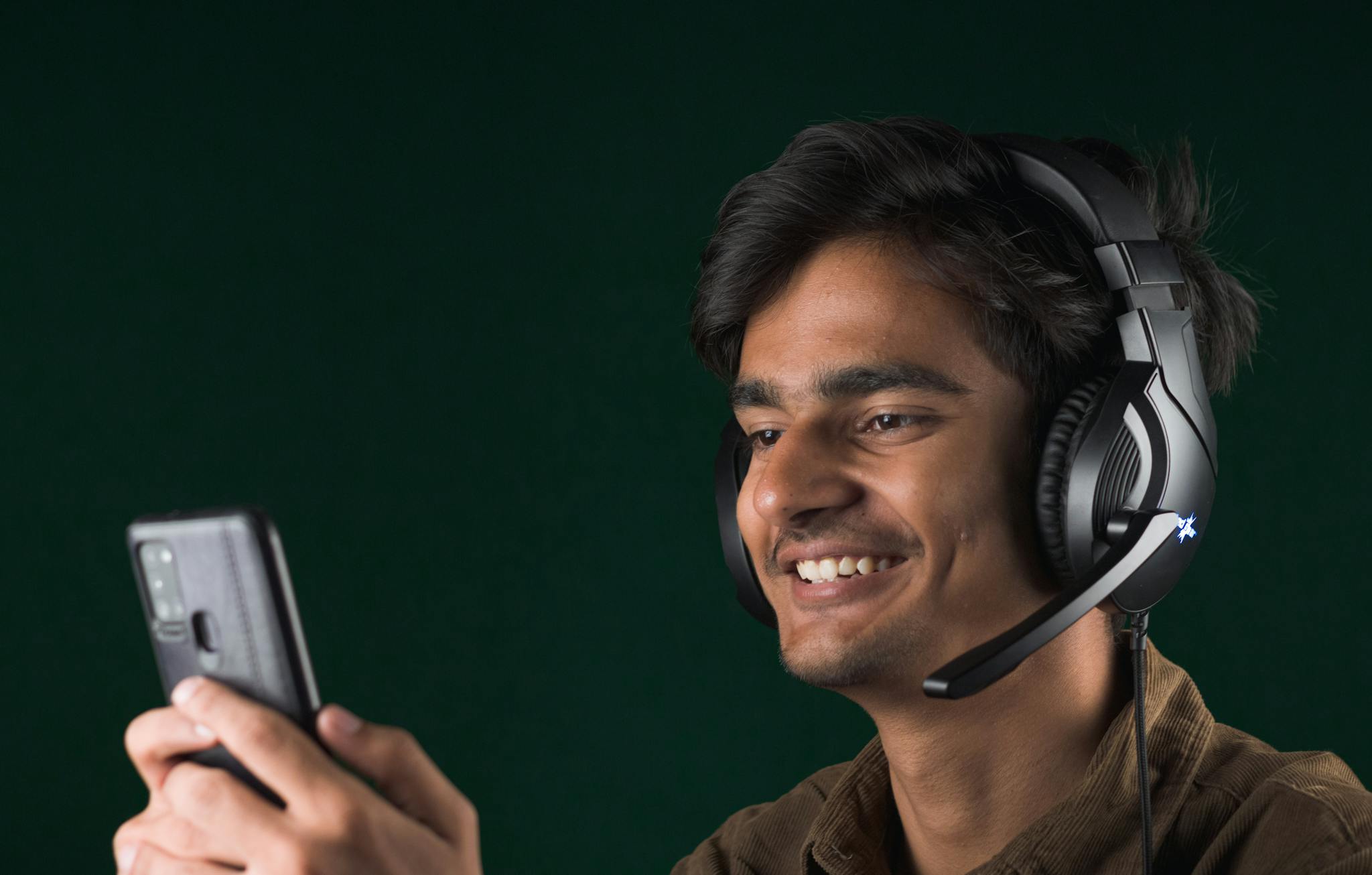 Smiling young man using a smartphone with headphones, enjoying music indoors.