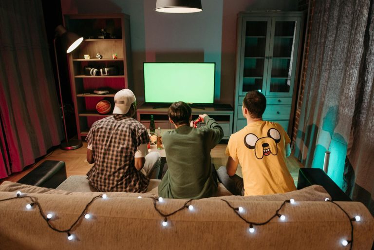 Three friends playing video games on a console in a cozy living room, viewed from behind